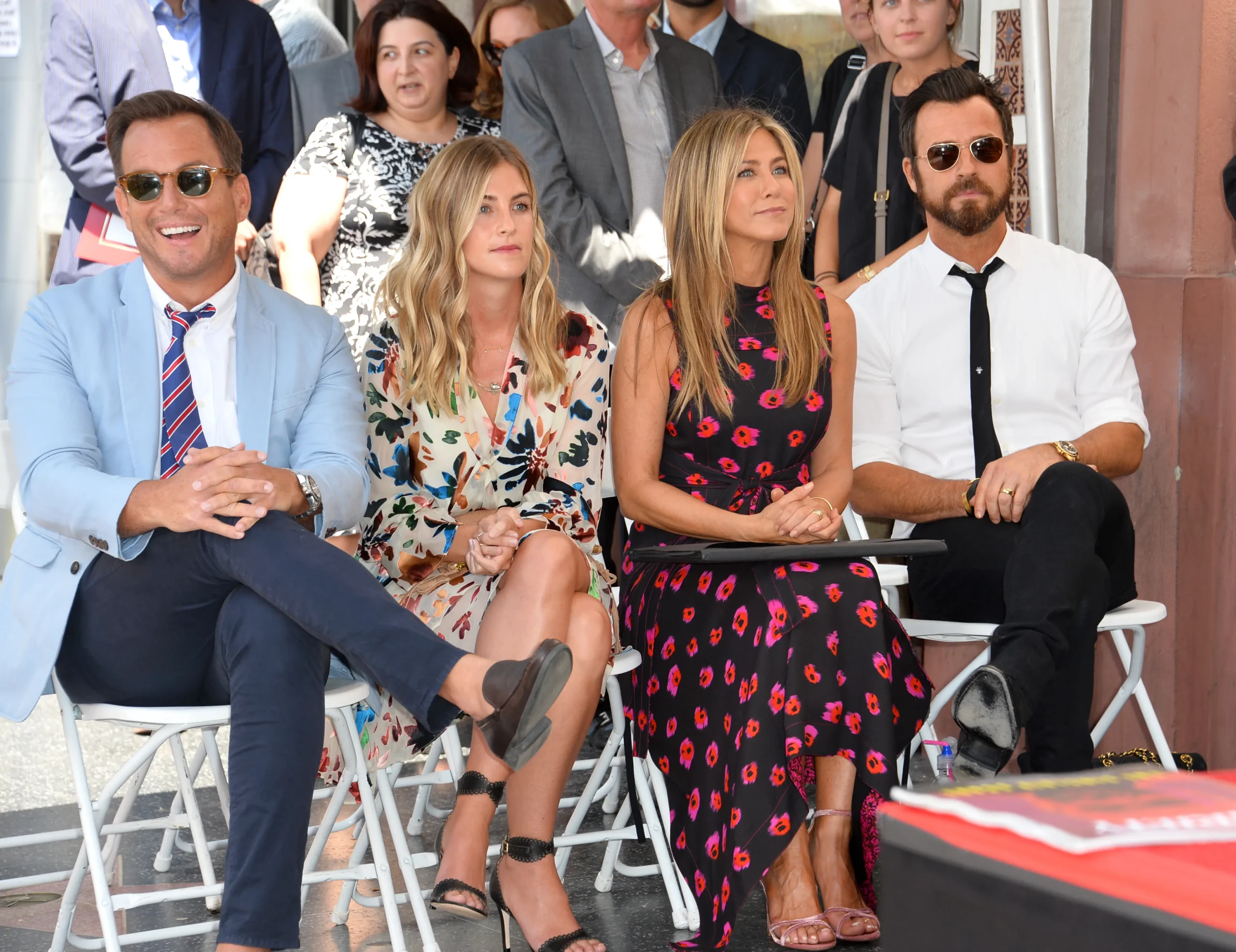 Jennifer Aniston sedí mezi lidmi.