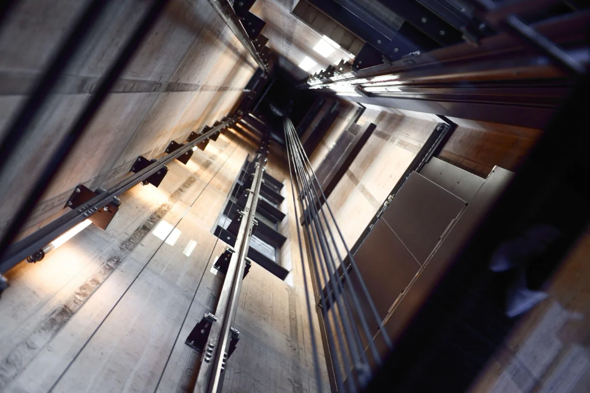 shutterstock_1979883002 1 | TVGURU.cz Perspective inside a concrete elevator shaft with steel rails, tracks and hanging cables.