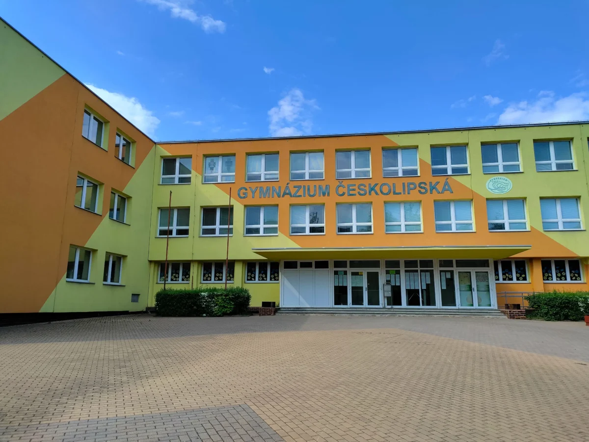 shutterstock_2163807343 1 | TVGURU.cz Colorful school building with orange and lime panels and a sign reading'GYMNÁZIUM ČESKOLIPSKÁ' against a clear blue sky.