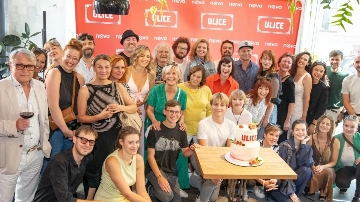 Group of people posing for a celebratory photo around a table with a two-tier cake, in front of a red ULICE backdrop.
