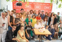Group of people posing for a celebratory photo around a table with a two-tier cake, in front of a red ULICE backdrop.