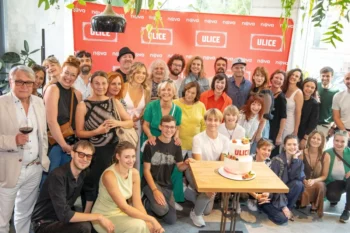 Group of people posing for a celebratory photo around a table with a two-tier cake, in front of a red ULICE backdrop.