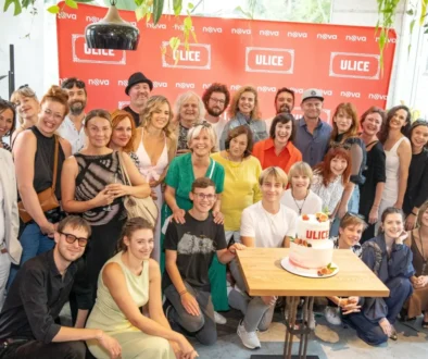Group of people posing for a celebratory photo around a table with a two-tier cake, in front of a red ULICE backdrop.