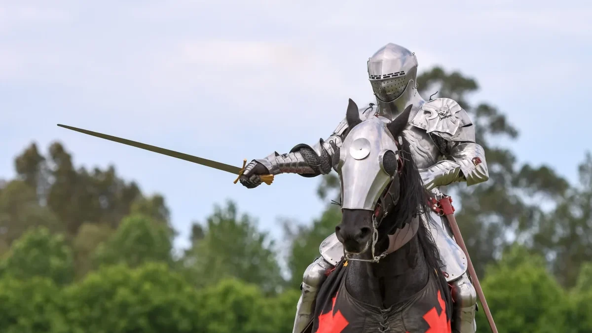Knight in full plate armor on a horse, sword drawn, outdoors in a grassy area.