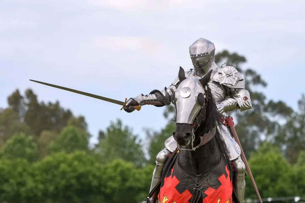 Knight in full plate armor on a horse, sword drawn, outdoors in a grassy area.