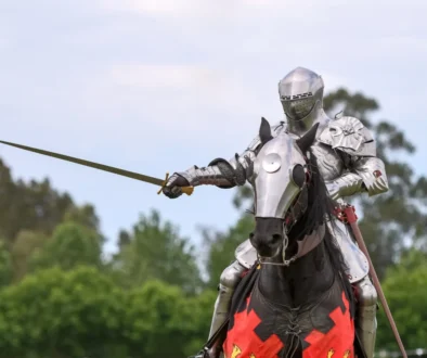 Knight in full plate armor on a horse, sword drawn, outdoors in a grassy area.