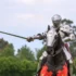 Knight in full plate armor on a horse, sword drawn, outdoors in a grassy area.