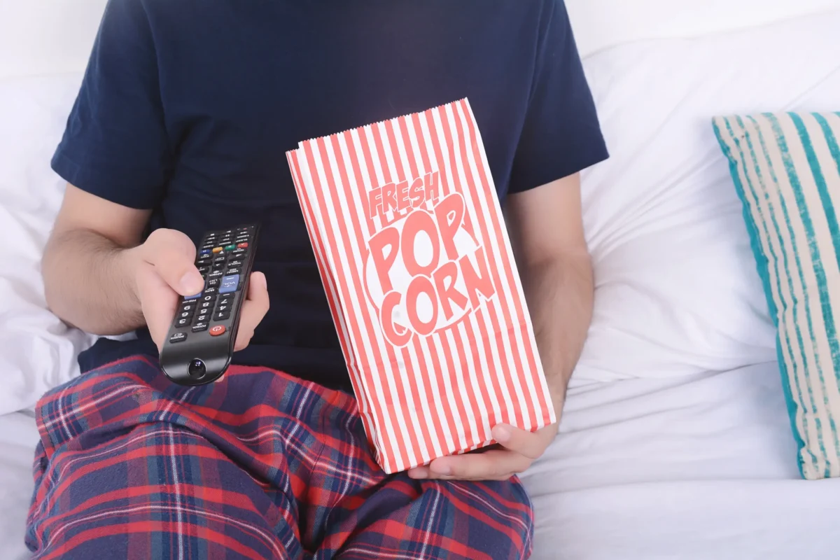 Člověk drží ovladač a popcorn.