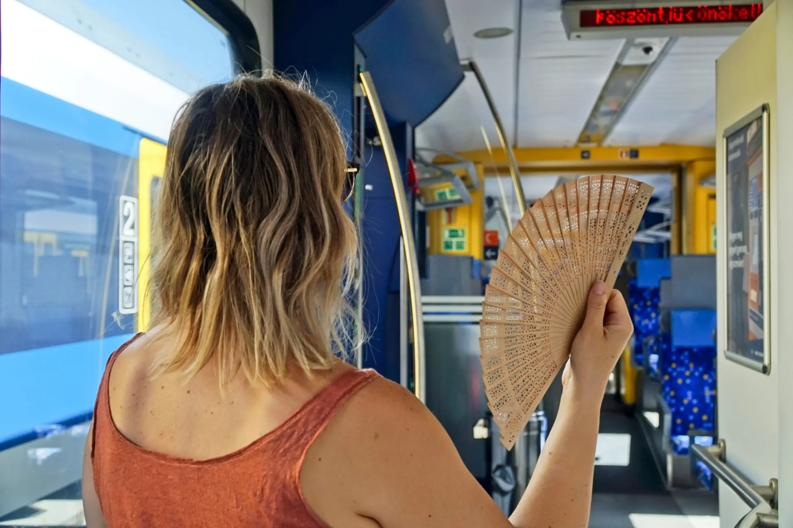 Žena se ovívá vějířem v tramvaji.