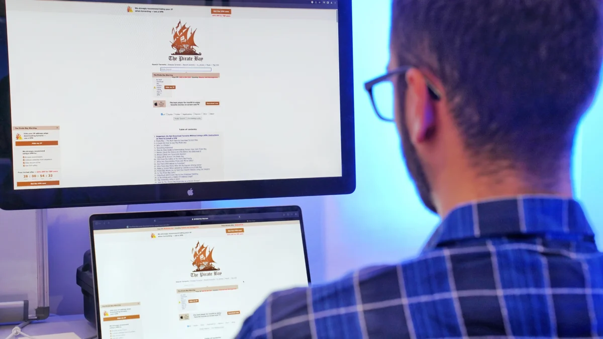Za nelegální šíření filmů může být udělena vysoká pokuta. Zdroj: Shutterstock | TVGURU.cz Muž sedící před počítačem se dvěma obrazovkami