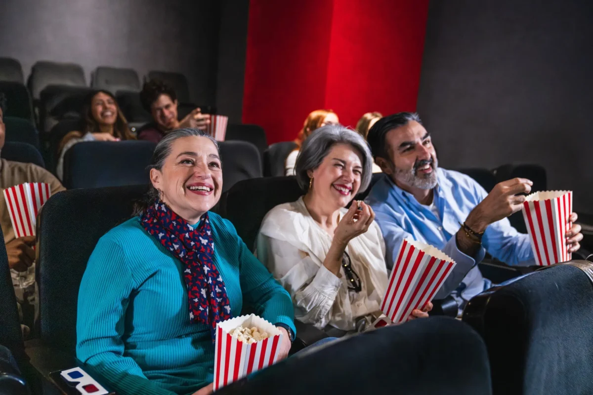 Návštěva kina je stále dražší záležitostí. Zdroj: Shutterstock | TVGURU.cz Dvě ženy a muž, kteří jedí v kině popcorn.