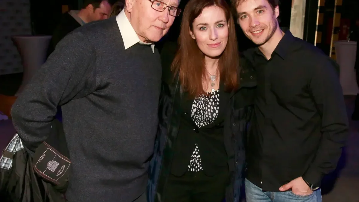 Three people pose for a photo together: an older man on the left, a woman in the middle, and a younger man on the right, smiling at the camera.
