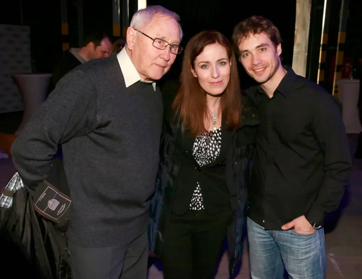 Three people pose for a photo together: an older man on the left, a woman in the middle, and a younger man on the right, smiling at the camera.