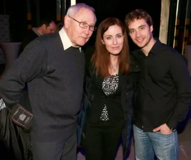 Three people pose for a photo together: an older man on the left, a woman in the middle, and a younger man on the right, smiling at the camera.