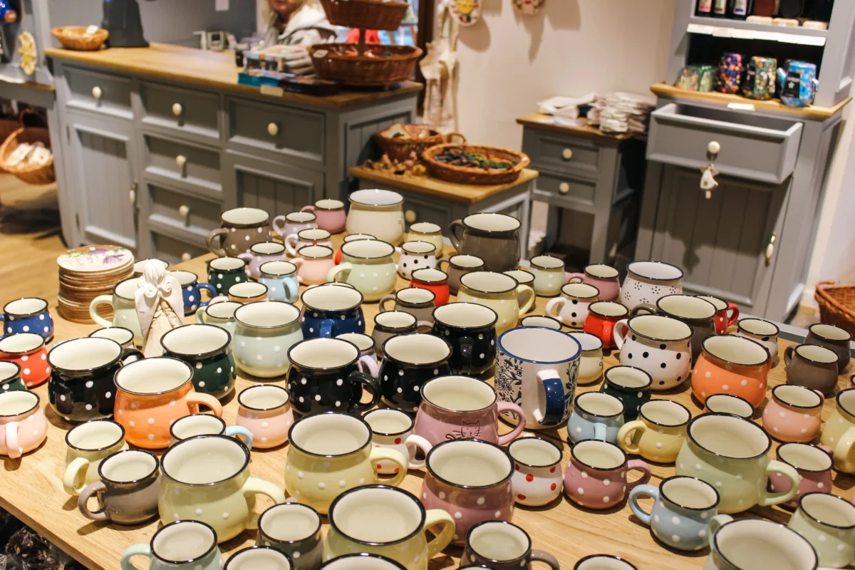 shutterstock_2790897499 1 | TVGURU.cz Colorful polka-dotted mugs on a wooden display table inside a kitchenware shop, with shelves in the background.