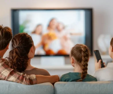 Family seated on a sofa watching a blurry TV show together, one person holding a remote control to the right