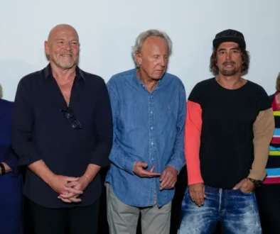 Group of six adults posing for a photo at an event, wearing casual outfits and standing shoulder to shoulder against a plain backdrop.