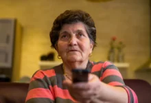 Babička před sebe míří televizním ovladačem.
