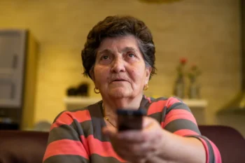 Babička před sebe míří televizním ovladačem.