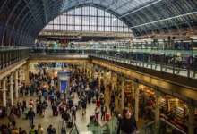 Busy train station concourse filled with travelers and luggage beneath a glass vaulted roof.