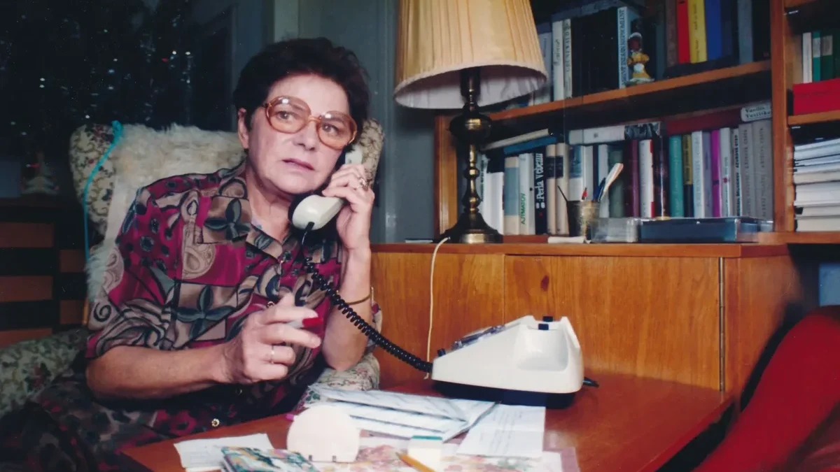 Jiřina Švorcová sedí u stolu a telefonuje.