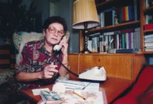 Jiřina Švorcová sedí u stolu a telefonuje.
