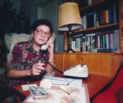 Jiřina Švorcová sedí u stolu a telefonuje.