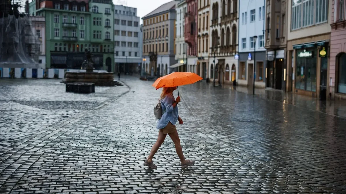 žena s oranžovým deštníkem přechází náměstí v česku