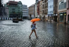 žena s oranžovým deštníkem přechází náměstí v česku