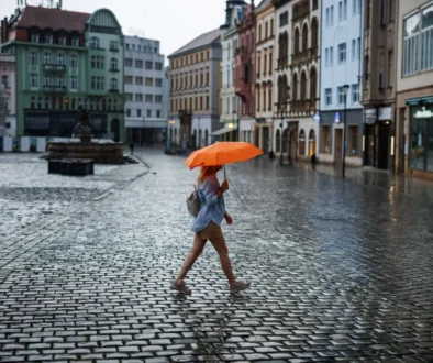 žena s oranžovým deštníkem přechází náměstí v česku