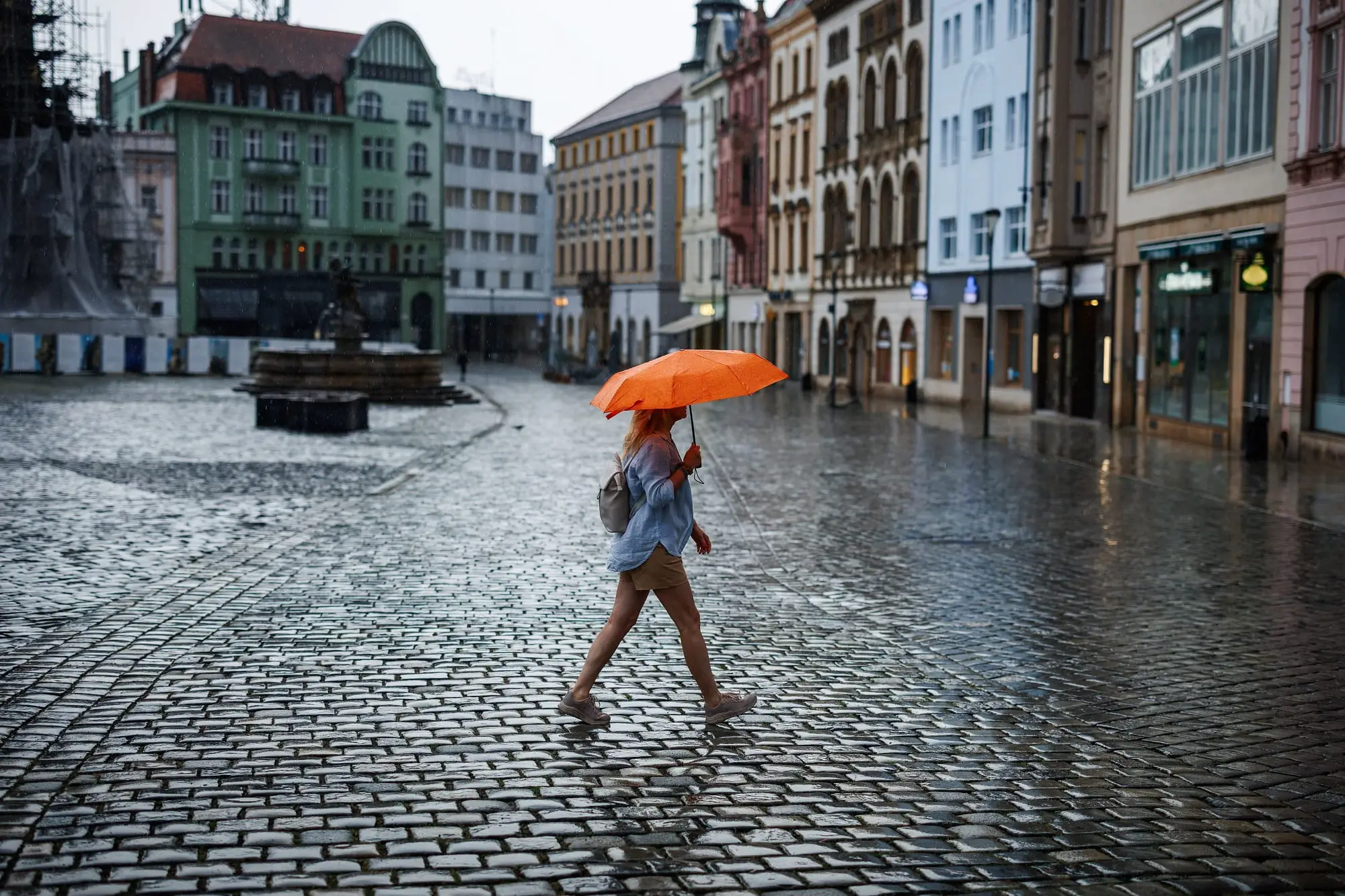 žena s oranžovým deštníkem přechází náměstí v česku