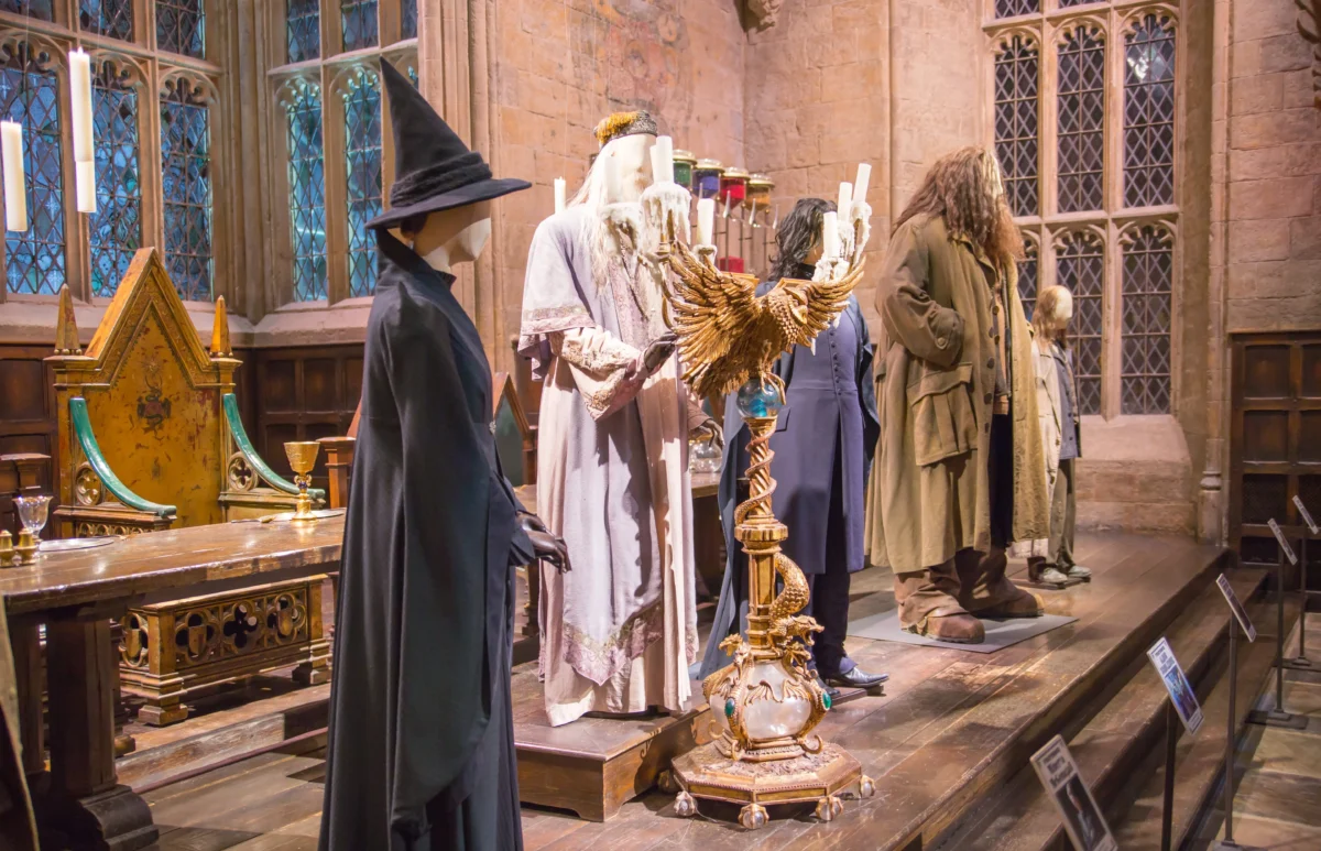 shutterstock_529072006 1 | TVGURU.cz Life-size mannequins in wizard robes and magical props on a display stage in a Gothic-style room with candles and stained glass windows far in the background, as in a museum exhibit.