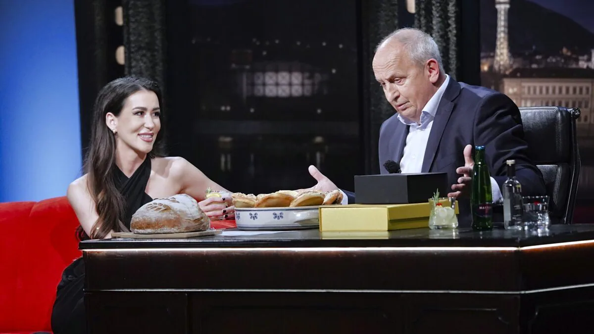 Prostředí televizní talk show s usmívající se hostující ženou a moderátorem u stolu, na stole viditelný chléb, pečivo a nápoje. V popředí s Janem Krausem