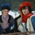 Two costumed men in a snowy outdoor setting, wearing medieval-style robes and hats, looking off to the side.