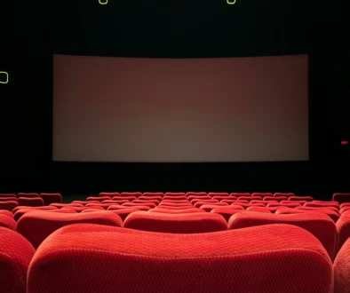 Empty red-velvet theater seats facing a large blank screen on a dark stage.