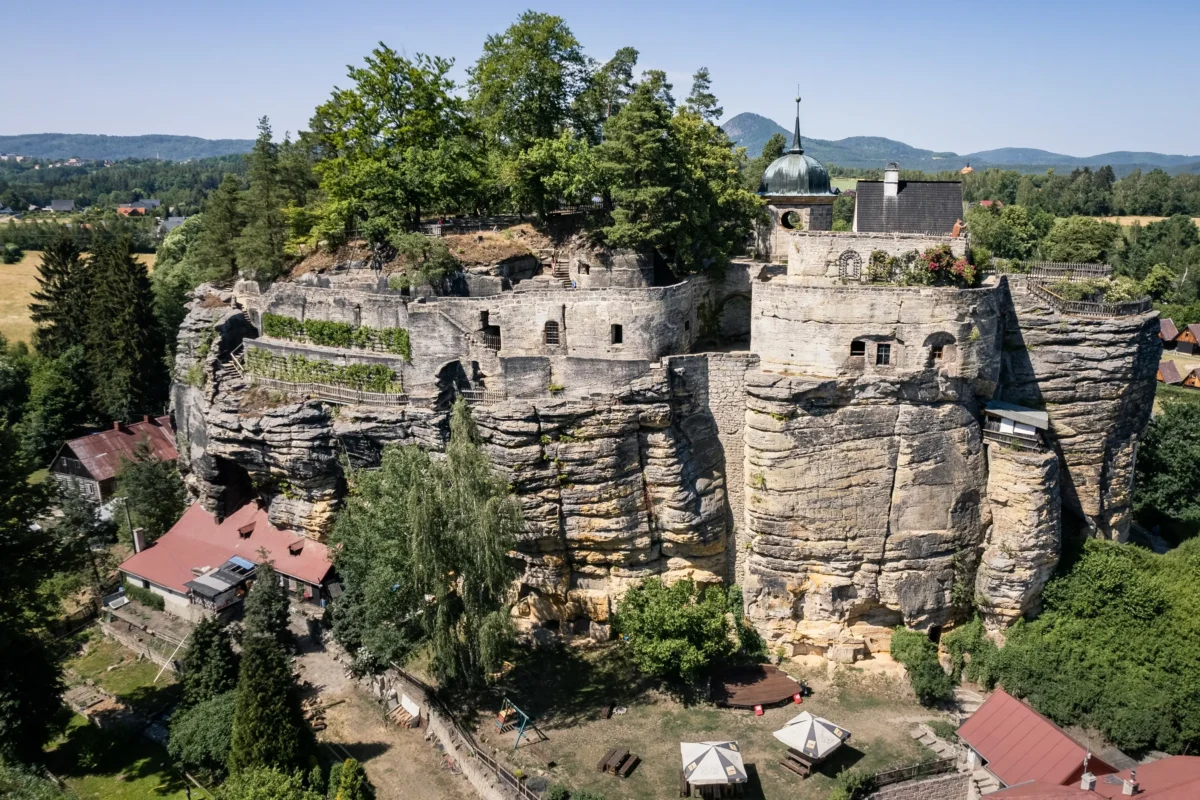 Hrad na skalnatém útesu s kamennými zdmi, kupolovitou věží a okolními stromy s výhledem na venkovskou krajinu (letecký pohled).