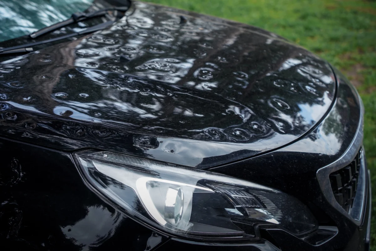 shutterstock_2653279861 1 | TVGURU.cz Close-up of a black car hood with water droplets after rain, wipers resting on the windshield edge and glossy reflections visible.