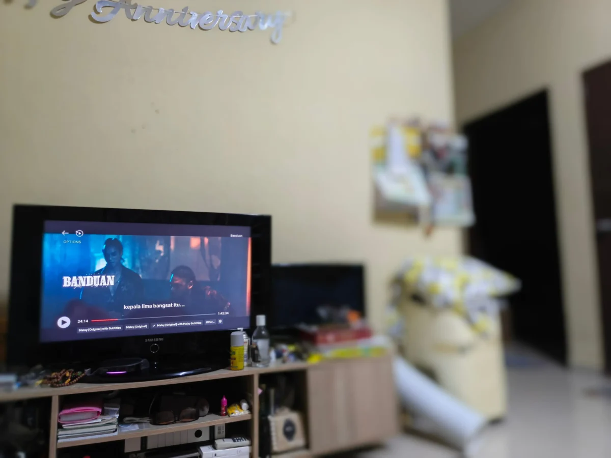 shutterstock_2752056873 2 1 | TVGURU.cz Blurred desk setup with a Samsung monitor playing a film titled Banduan; shelves and clutter in the background.