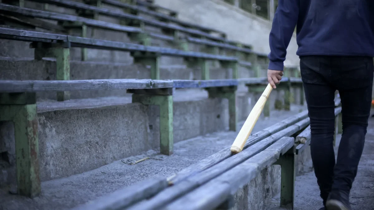 Muž jde podél laviček s baseballovou pálkou.