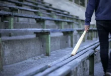 Muž jde podél laviček s baseballovou pálkou.
