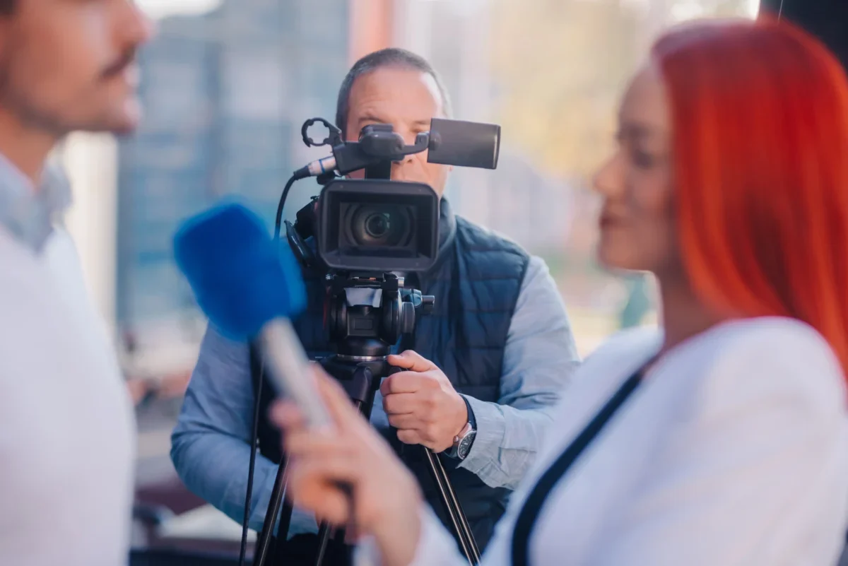 Muž stojí za kamerou a natáčí reportáž.