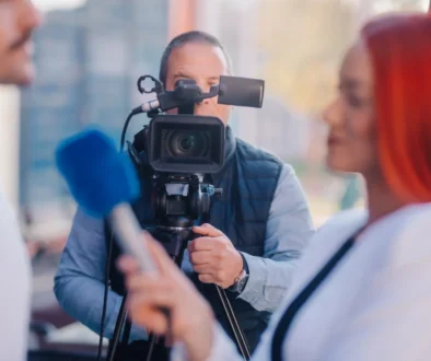 Muž stojí za kamerou a natáčí reportáž.