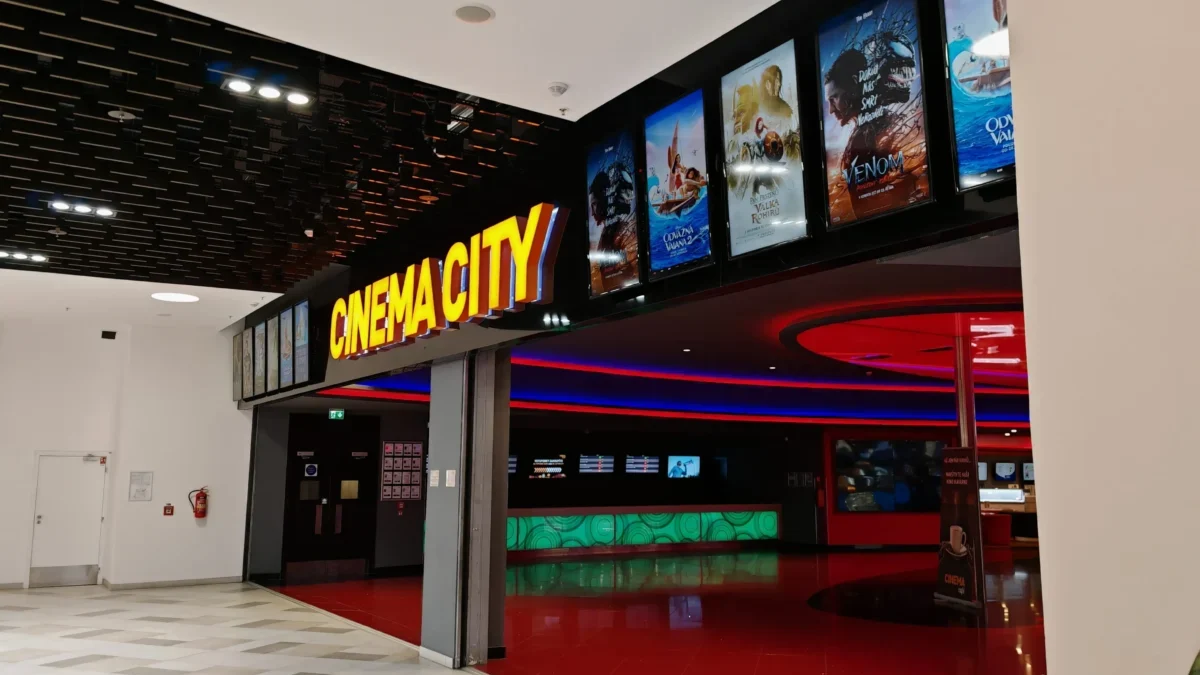 Cinema lobby with a bright yellow 'CINEMA CITY' sign and film posters along a black wall.