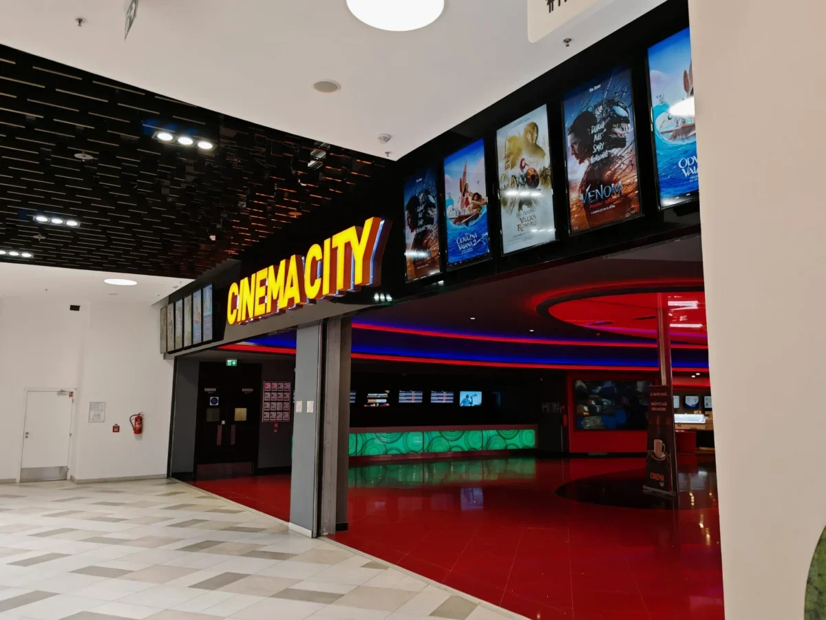 Cinema lobby with a bright yellow 'CINEMA CITY' sign and film posters along a black wall.