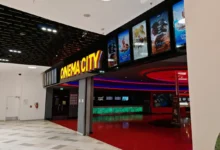Cinema lobby with a bright yellow 'CINEMA CITY' sign and film posters along a black wall.