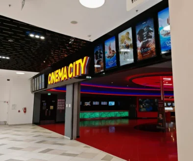 Cinema lobby with a bright yellow 'CINEMA CITY' sign and film posters along a black wall.