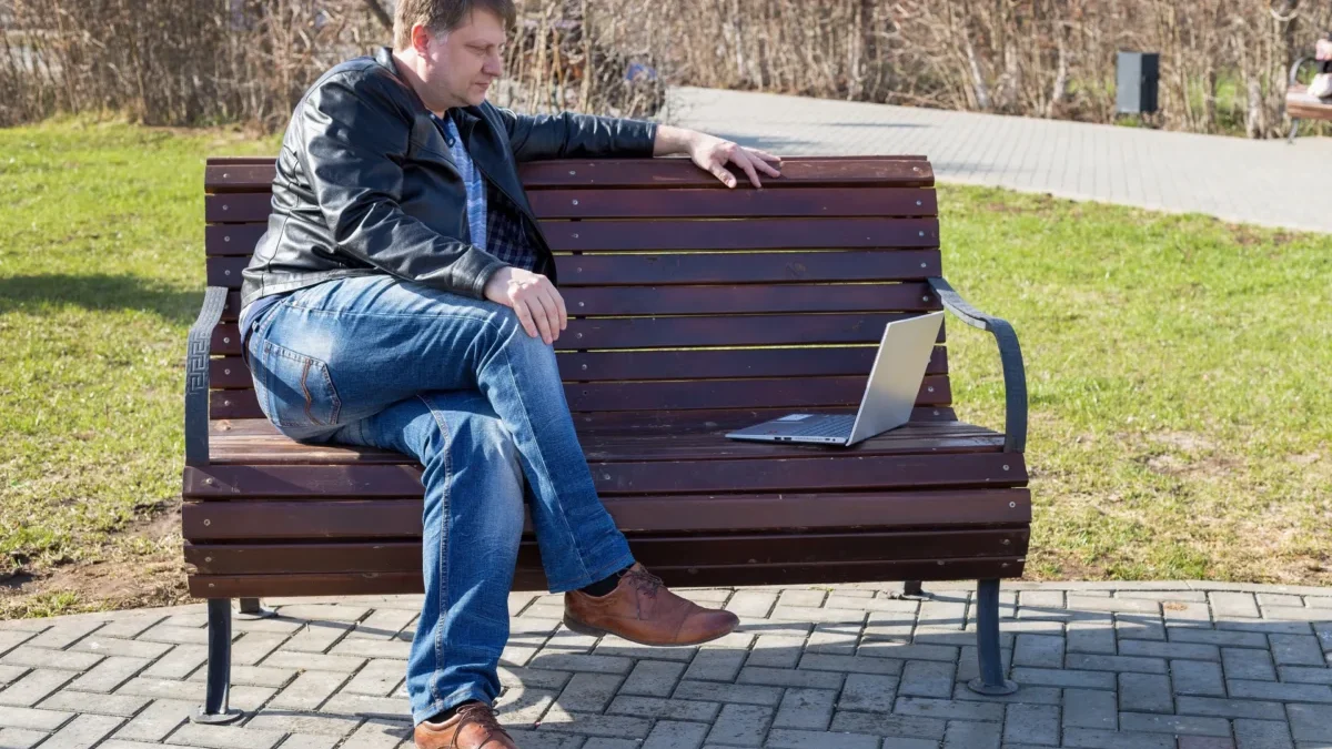 Muž sedí s notebookem na lavičce.