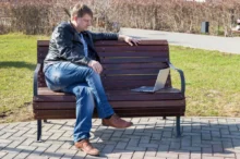 Muž sedí s notebookem na lavičce.