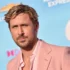 Close-up portrait of a man with blond hair and light stubble wearing a pink suit, photographed outdoors against a blue event backdrop.