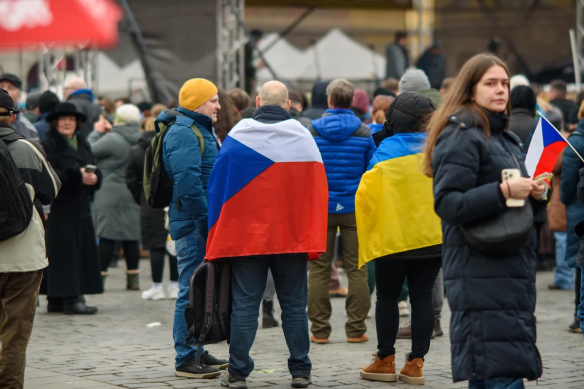 Lidé stojí venku a jsou omotaní vlajkami.